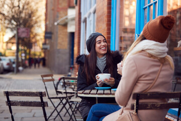 Two Female Friends Meeting Sitting Outside Coffee Shop On City High Street