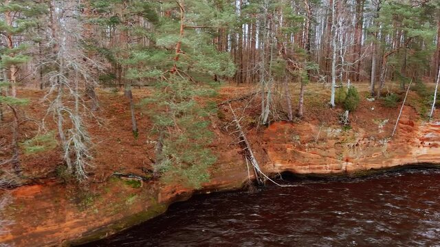 Red sandstone cliffs in the banks of river Salaca during late autumn time, Latvia. Real time drone footage