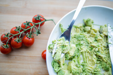 Cherry tomatoes and bowl of mashed avocado on wooden table