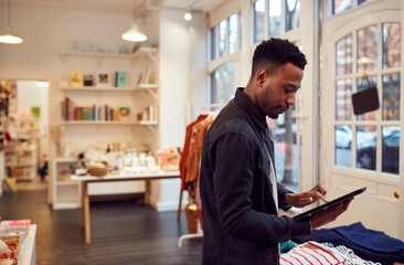 Male Small Business Owner Checks Stock In Shop Using Digital Tablet