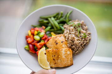 Hand holding salmon and buckwheat dish with green beans