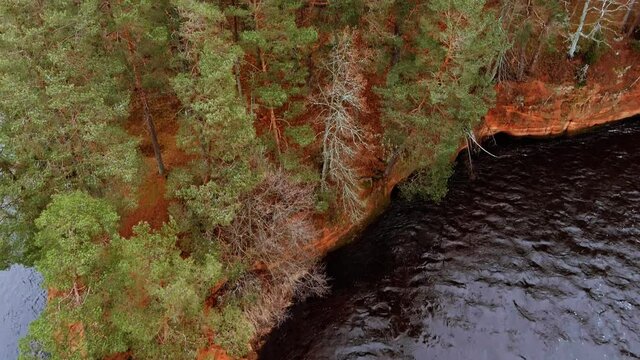 Red sandstone cliffs in the banks of river Salaca during late autumn time, Latvia. Real time drone footage