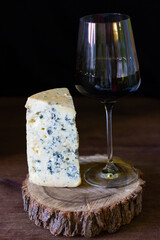 a piece of blue roquefort cheese and a glass of red wine on a wooden frame on a wooden background in rustic style