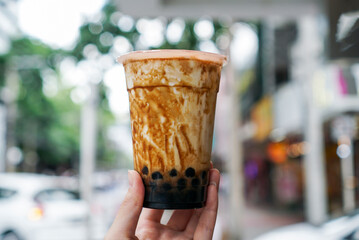 Bubble brown sugar Milk Tea. Holding a plastic cup of milk tea with bubble/boba (black pearl) and...