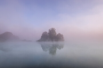Fototapeta premium island in lake on foggy autumn morning, reflected in water.