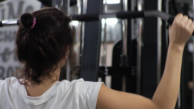 Gym. Lesson with a young funny trainer man. A beginner young woman shakes her back and arms on the simulator.