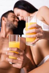close up view of glasses with juice in hands of smiling young couple on blurred background