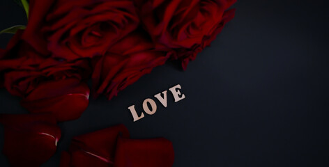 Word love in wooden letters near a bouquette of red roses on dark grey background. Banner. St. Valentines card.