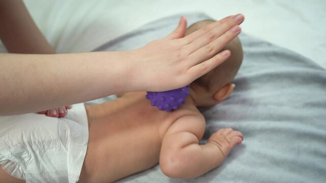 Female hands massage the back of a newborn baby using a rubber ball with spikes