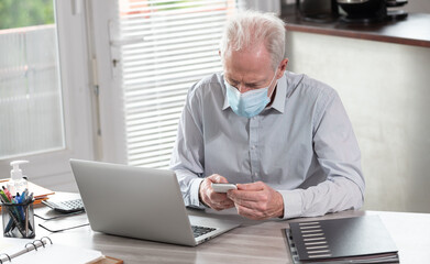 Businessman wearing medical face mask and using mobile phone from home