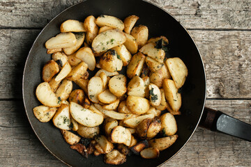 Frying pan full of fried potatoes on the old rough wooden boards. Above view