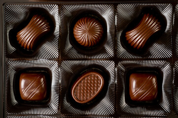 Assorted chocolates lying in a box. Background for products from chocolate and sweets. Dark chocolate.