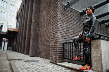 Fototapeta na wymiar Fashionable beautiful african american woman posing in black leather jacket and pants at street.