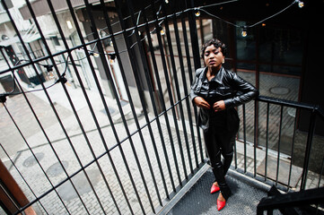 Fashionable beautiful african american woman posing in black leather jacket and pants at street.