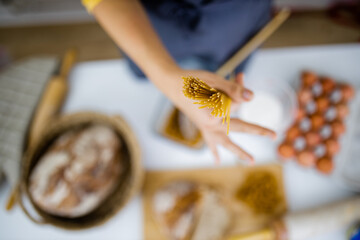 Female hand holding uncooked spaghetti above ingredients on a table