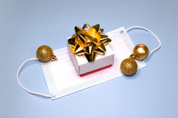 Gift box decorated with a bow with gold balls and a mask on a blue background