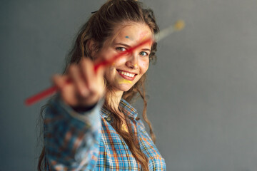 Fototapeta premium Smiling female artist standing next to the camera with a brush for painting in the studio. A professional female painter draws in a workshop.