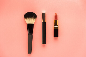 lipstick, makeup brush, mascara on a pink surface top view