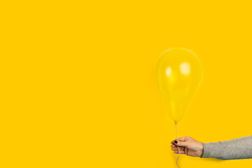 Mano de mujer sosteniendo un globo amarillo sobre un fondo amarillo liso y aislado. Vista de...