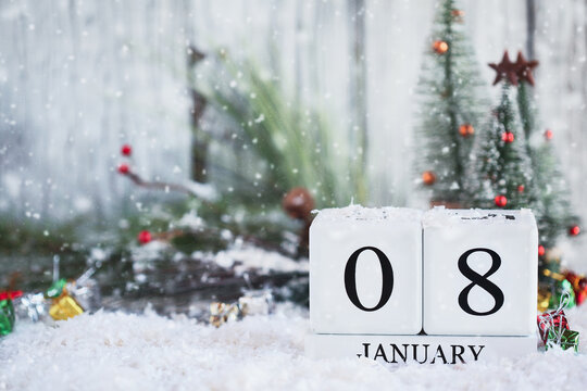 White wood calendar blocks with the date January 8th and Christmas decorations with snow. Selective focus with blurred background. 