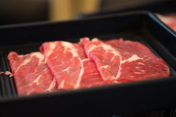 Raw sliced Wagyu beef for shabu shabu on black tray.