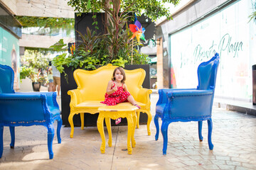 Happy and adorable little girl on a yellow armchair in an alley