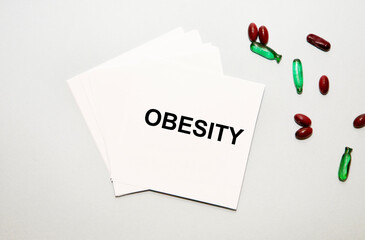 On the sheets for notes the text of OBESITY, next to the capsule red and green.