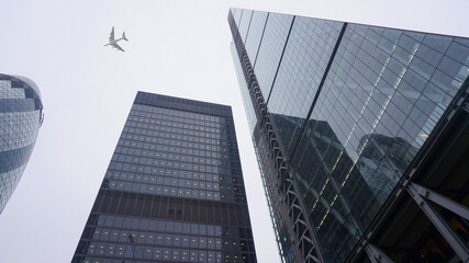 Fototapeta premium Ground level view of passenger airplane flying at high altitude above London city skyline, financial district, United Kingdom