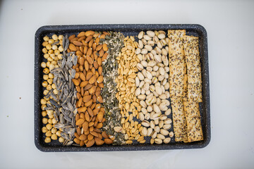 Black tray of nuts and seeds above a white table