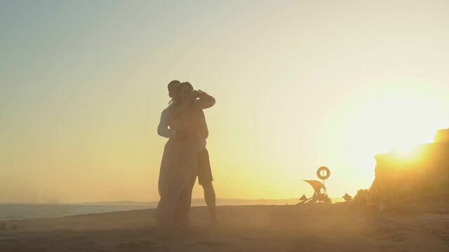 Newlyweds, a young couple at a romantic meeting on the seashore at sunset dancing in slow motion.