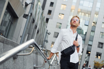 Young elegant man in good clothes is outdoors in the city at daytime