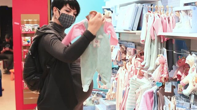 Examines the material of the goods with his hands. Consumption of goods. Woman in mask with a big belly pregnancy chooses goods to buy in the store. Shopping at the supermarket. 