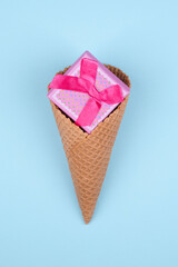 Pink gift box in ice cream cone on light blue background. Minimal Valentines day concept.