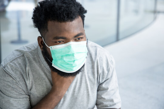 Symptometic black african man wearing hygienic face mask and having sore throat due to covid-19 flu symptom