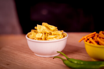 Papdi Gathiya in white bowl with onion and chili peppers on table,namkeen Food Ghatiya and papdi also know as Ganthiya or Gathiya, selective focus