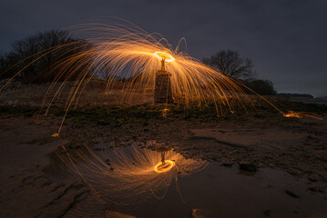Sparks, Fire and a halo of light falling to a beach and reflected in a pool of water