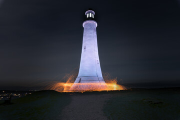 Fire and sparks surround the base of a lighthouse perched on top of a hill