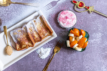 Traditional french toast with cinnamon on a gray background. Traditional Spanish sweet fried toasts, torrijas, with banana and persimmon, fresh cream, powdered sugar on a ceramic plate, and gold
