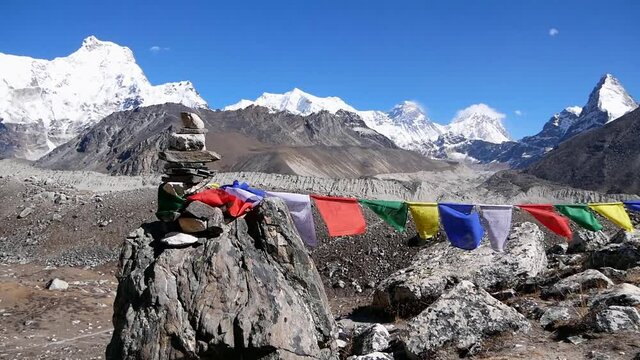Colorful Buddhist prayer flags tied to pile of stones flying in cold wind in upper Gokyo valley, Sagarmatha National Park, Nepal with stunning mountain panorama including Mount Everest (8,848 m).