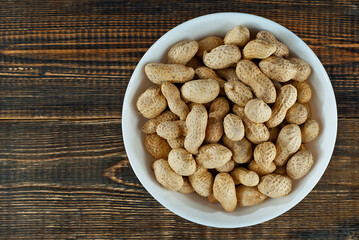 Peanuts in a white bowl on an old shabby board. Nuts on a brown wooden table.
