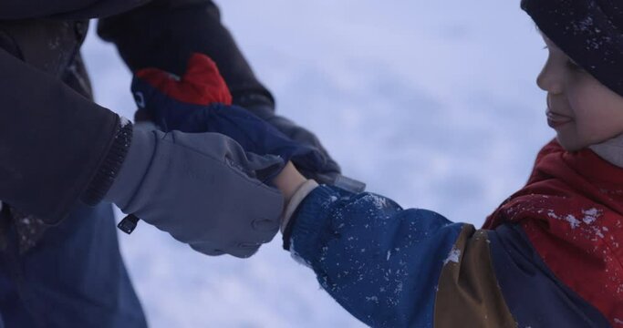 Father helps young son put on winter mittens outdoors in snow