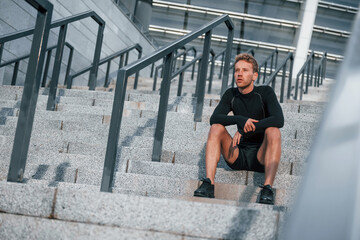 Takes a break. Young man in sportive clothes have workout outdoors at daytime