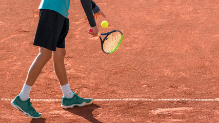 Professional tennis player on red clay tennis court prepares to serve. Athlete with tennis racket and ball. Start of match, game, set. Sports panoramic background or banner with copy space.