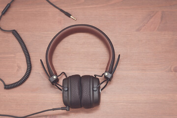 Brown design headphones with wire on wooden background.