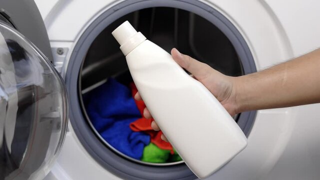 A man with a bottle of laundry detergent About to pour the detergent into the washing machine
