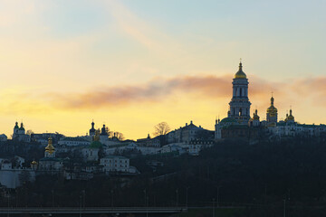 Fototapeta premium Scenic winter landscape view of famous Kyiv's hills against cloudy sky during sunset. Scenic landscape of ancient Kyiv Pechersk Lavra. It is a historic Orthodox Christian monastery. Kyiv, Ukraine