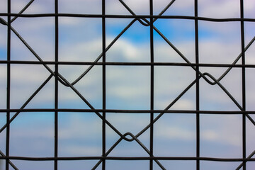 Metal protective grid or netting against a background of blue sky with white clouds. Protected facility, parking lot or prison. High quality photo