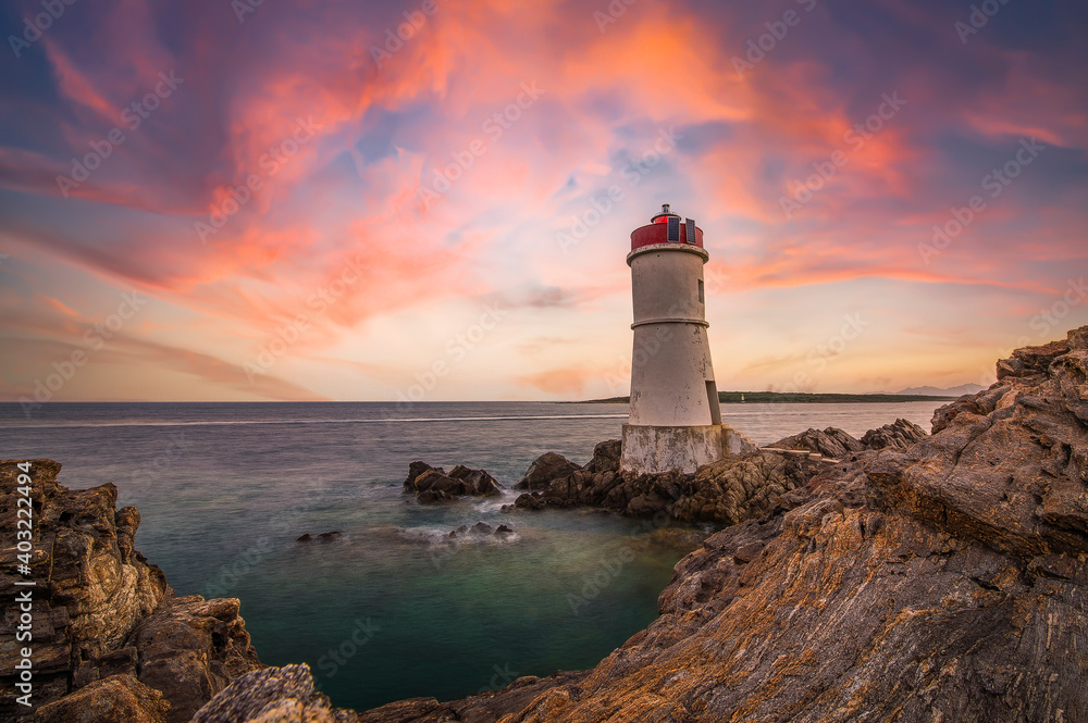 Wall mural (Selective focus) Stunning view of a rocky coastline with a lighthouse during a dramatic sunset. Sardinia, Italy - Wall murals
