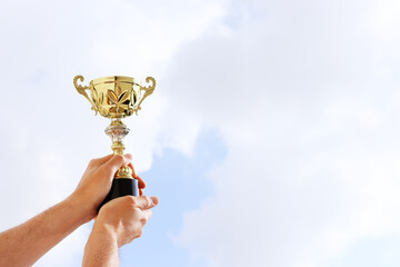 Man holding up a trophy cup as a winner against the blue sky. Award and victory concept