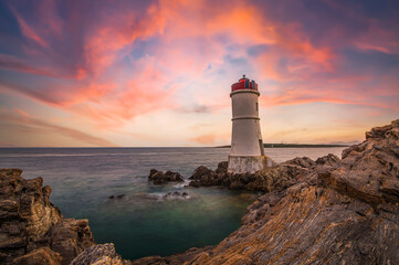 (Selective focus) Stunning view of a rocky coastline with a lighthouse during a dramatic sunset. Sardinia, Italy